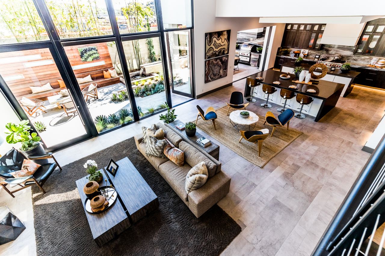 Open living area seen from the loft above, with a wall of glass onto a landscaped patio